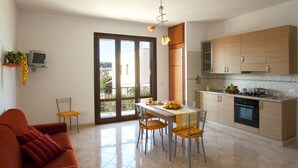 A modern kitchen with a dining area, featuring a large window, a sofa, and a TV on a shelf. - Brand new Rossoarancio apartment with panoramic terrace (San Vito Lo Capo)