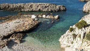A rocky coastal landscape with clear water, rugged terrain, and sparse vegetation. - Brand new Rossoarancio apartment with panoramic terrace (San Vito Lo Capo)