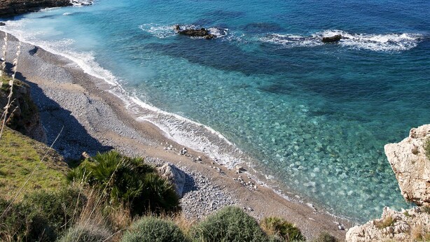 A coastal landscape with clear blue waters, a pebbly beach, and rocky cliffs. - Brand new Rossoarancio apartment with panoramic terrace (San Vito Lo Capo)
