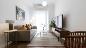 A modern living room with a sofa, coffee table, TV, and a wooden chair. - Urbieta | The Rentals Collection (San Sebastián)