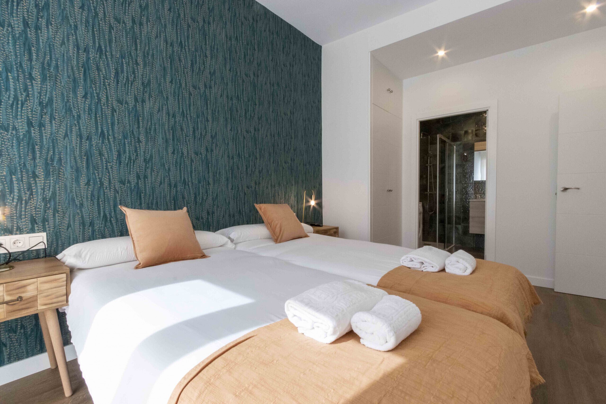 Une chambre d’hôtel avec deux lits, une table de chevet en bois, un miroir et une salle de bain avec une porte en verre.