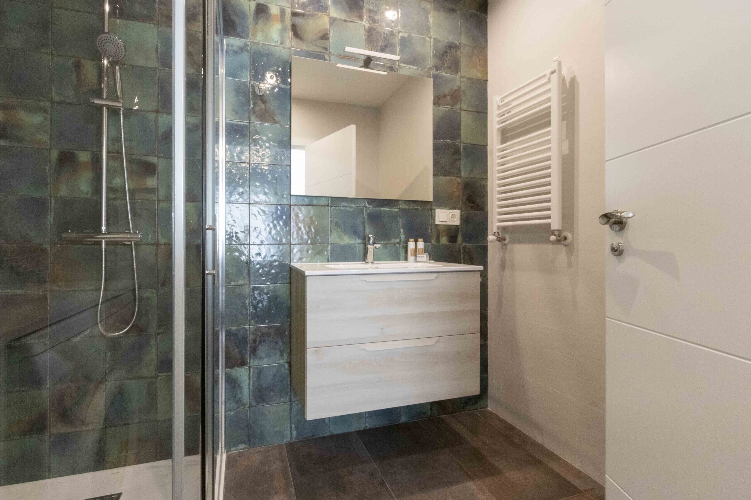 Un baño moderno con cabina de ducha de vidrio, un tocador blanco con espejo y un perchero de toallas en la pared.