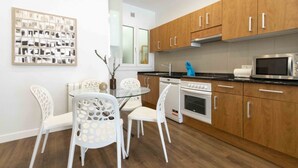 A modern kitchen with wooden cabinets, a microwave, and a dishwasher. There is a dining table with white chairs and a glass top. - Urbieta | The Rentals Collection (San Sebastián)