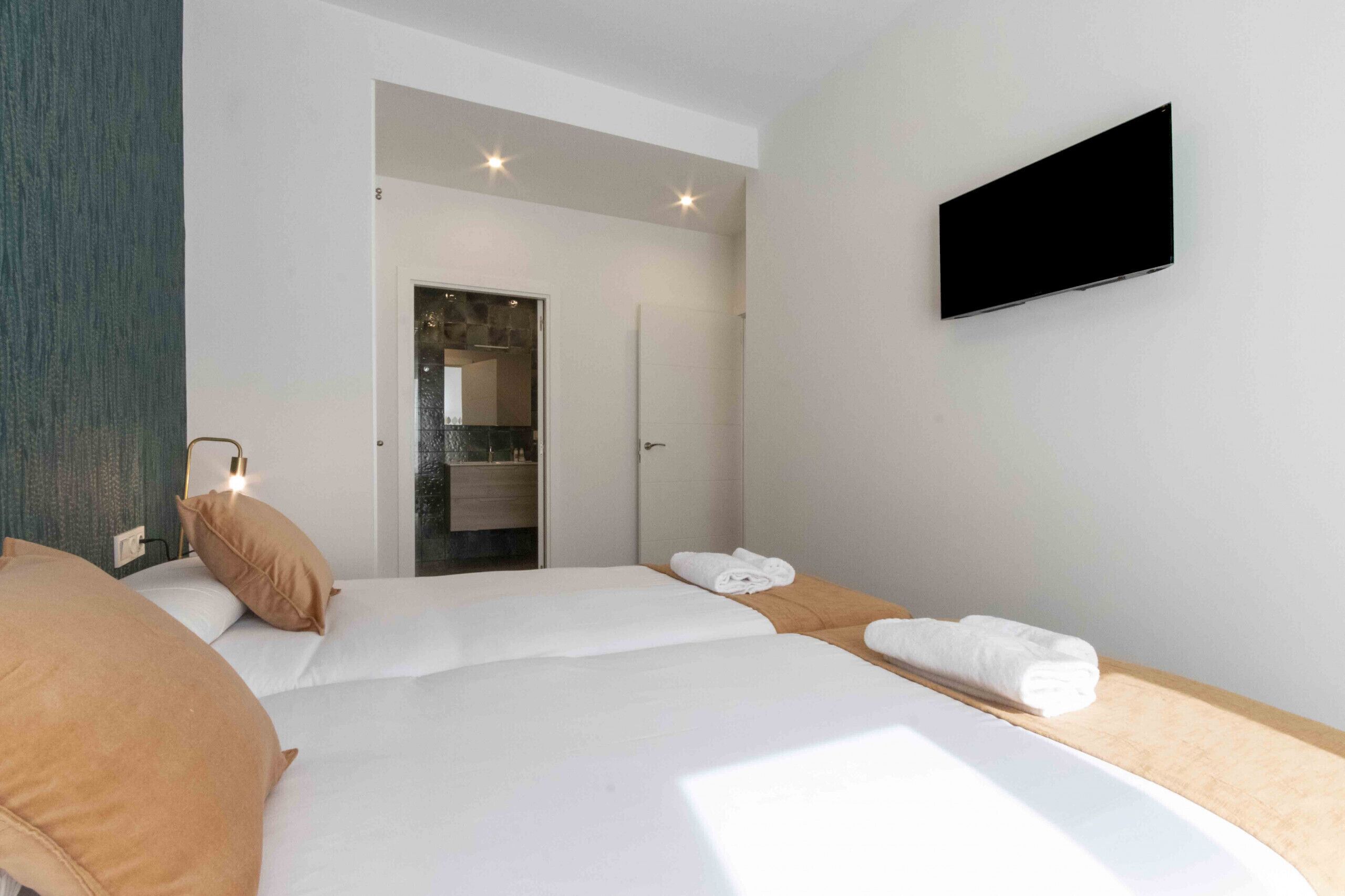 Ett hotellrum med två sängar, en tv som är monterad på väggen och ett badrum som syns genom en öppen dörr.