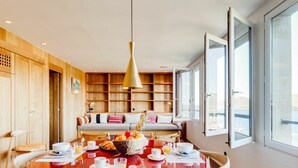 A dining area with a round table set for breakfast, a wooden bookshelf in the background, and a large window with a view. - Cosy apartment for 4 people with A/C, WIFI, TV and terrace (Porto-vecchio)