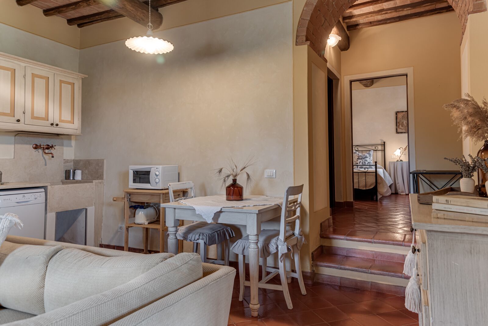 A cozy living room with a sofa, a dining table with chairs, a kitchen area with a microwave, and a staircase leading to another room.
