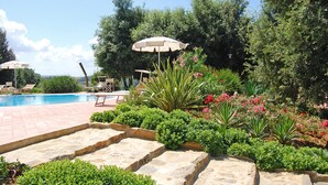 A pool area with stone steps, lounge chairs, and an umbrella.