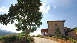 A stone house with a wooden porch, surrounded by a stone wall and a garden.
