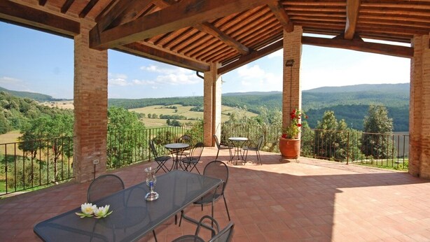 An outdoor patio with a table and chairs, a potted plant, and a view of the countryside.