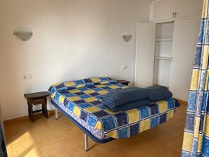 A bedroom with a bed, a small wooden nightstand, a wardrobe, and a curtain.