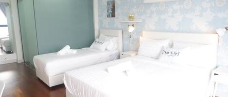 A hotel room with two beds, a glass partition, a world map wallpaper, and a shelf with decorative items.