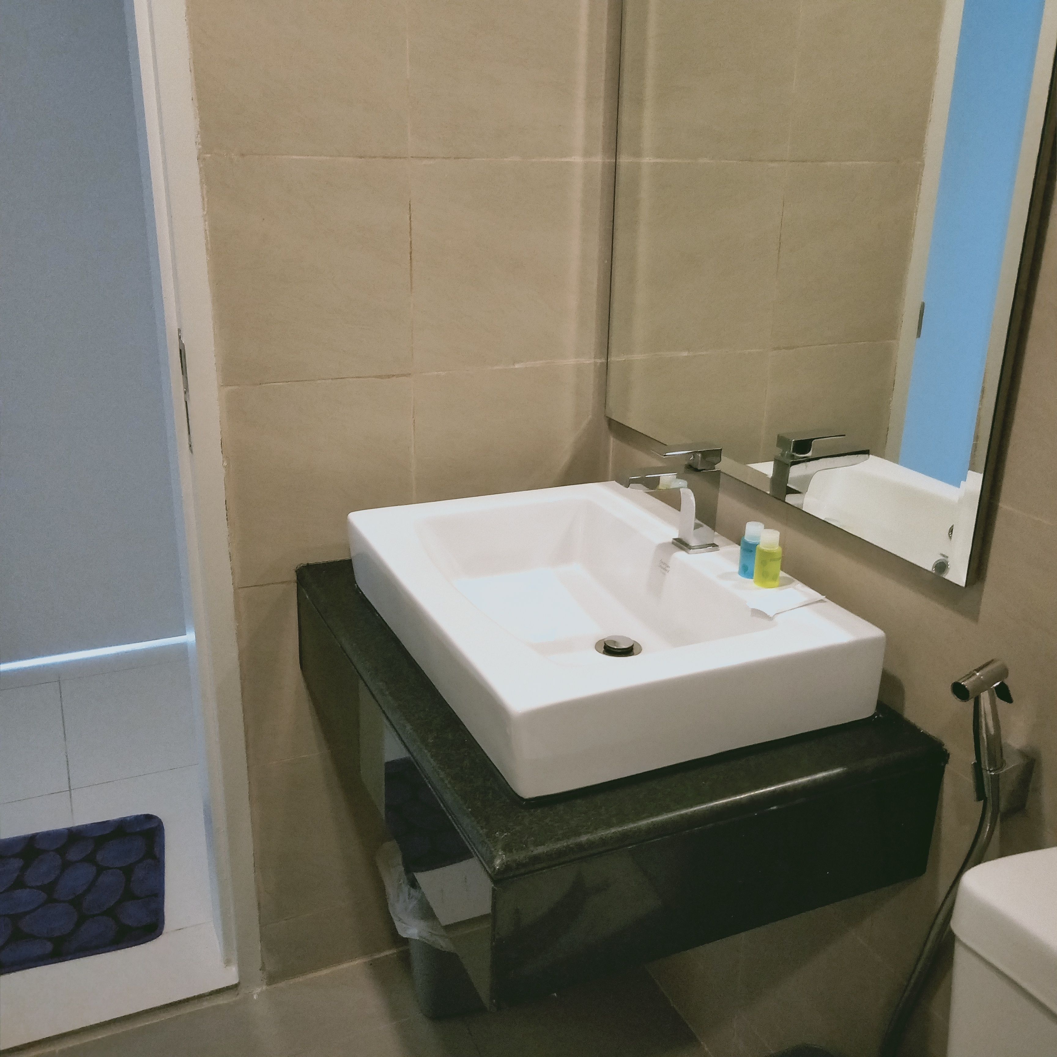 Une salle de bain avec un lavabo blanc, un miroir et un plan de toilette noir.