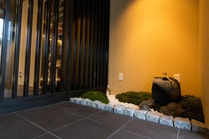 A modern interior with a dark floor, a glass partition, and a small garden area with rocks and white pebbles. - Hotel Japanesque Kyoto Station ZEQUU (Kyoto)