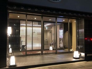 A hotel entrance with a modern design, featuring a glass door with vertical blinds, a reception desk, and a well-lit interior. - Hotel Japanesque Kyoto Station ZEQUU (Kyoto)
