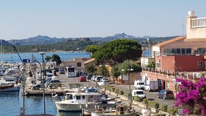 A marina with boats docked, a road with cars, and buildings with balconies overlooking the water.
