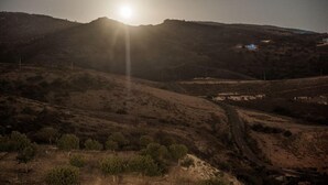 Un paisaje rural con un camino de tierra, vegetación escasa y un edificio distante con iluminación azul.