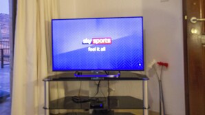 Una televisione a schermo piatto su un supporto in vetro in una stanza con una parete bianca e una porta.