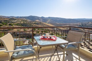 A balcony with two chairs and a table, a tray with cups and a pitcher, and a scenic view of hills and mountains.
