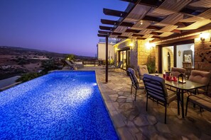 A swimming pool with a tiled edge, a patio area with outdoor furniture, and a view of the landscape. - 3 Bed, 3 Bath Modern Stone Villa with Private Infinity Pool (Paphos)