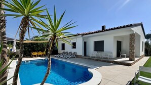 Una casa moderna con piscina, mobiliario exterior y un pilar de piedra.