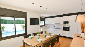 Una cocina moderna con armarios blancos, una mesa de comedor para cuatro personas y vistas al exterior a través de grandes ventanales.