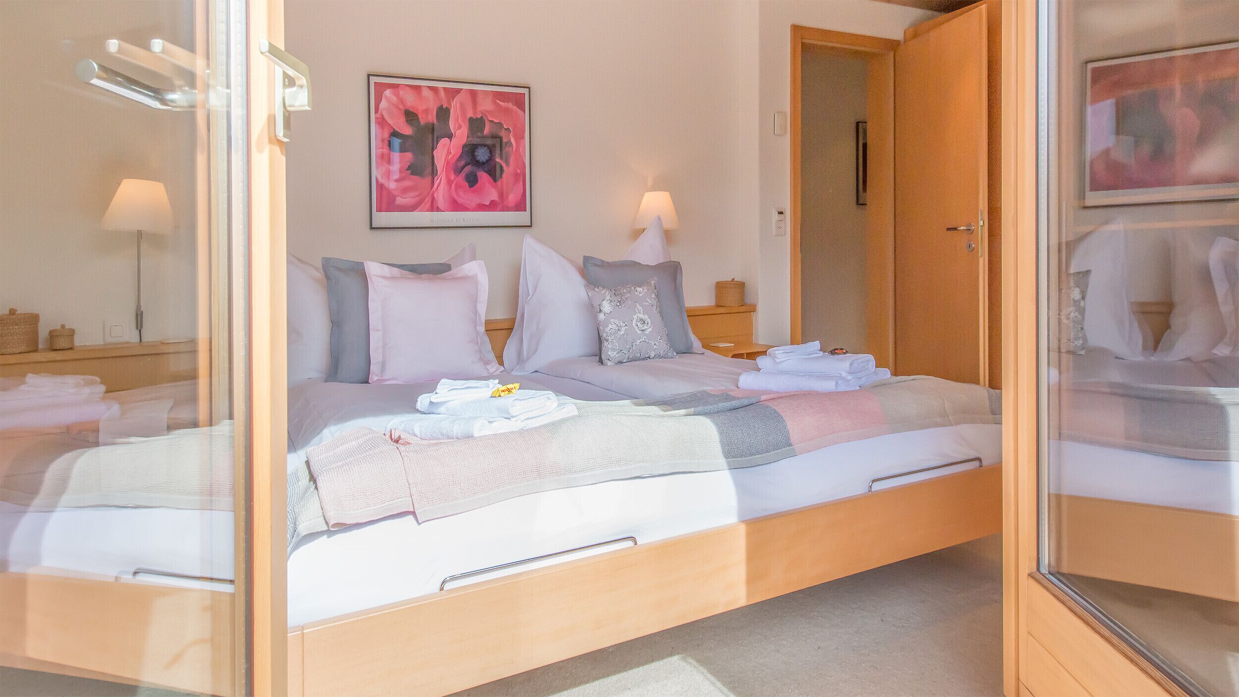 A neatly made bed with pillows and a blanket, a bedside lamp, a framed artwork on the wall, and a wooden door.