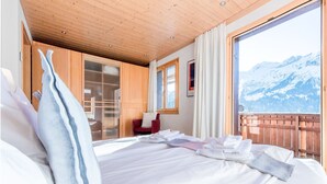 A hotel room with a large bed, a wooden ceiling, a red chair, and a view of snow-capped mountains.