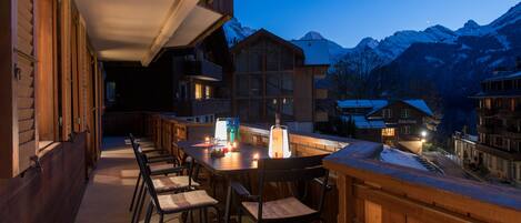 A wooden outdoor seating area with tables and chairs, overlooking a mountain range.