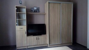 Ein Zimmer mit Fernseher auf einer Holzkommode, einem Kleiderschrank und einem Regal mit gerahmten Bildern.