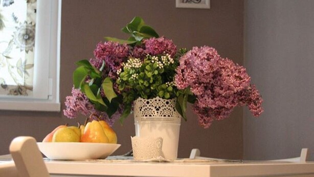 Ein Essbereich mit Tisch für zwei Personen, einer Blumenvase und einer Obstschale.