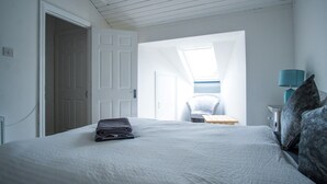 Een slaapkamer met een net opgemaakt bed, een stoel, een bureau en een lamp.