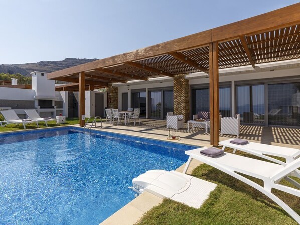Ein moderner Außenpoolbereich mit Liegestühlen, einer Pergola und Bergblick.