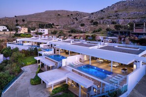 A modern hotel with multiple swimming pools, outdoor seating areas, and a view of the surrounding landscape.