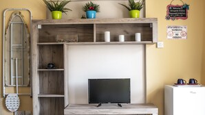 A compact living space with a wooden TV stand, a small refrigerator, and a shelf with decorative items. - Lucky 2 - Great location, close to the most beautiful beaches of Cyprus! (Paralimni)