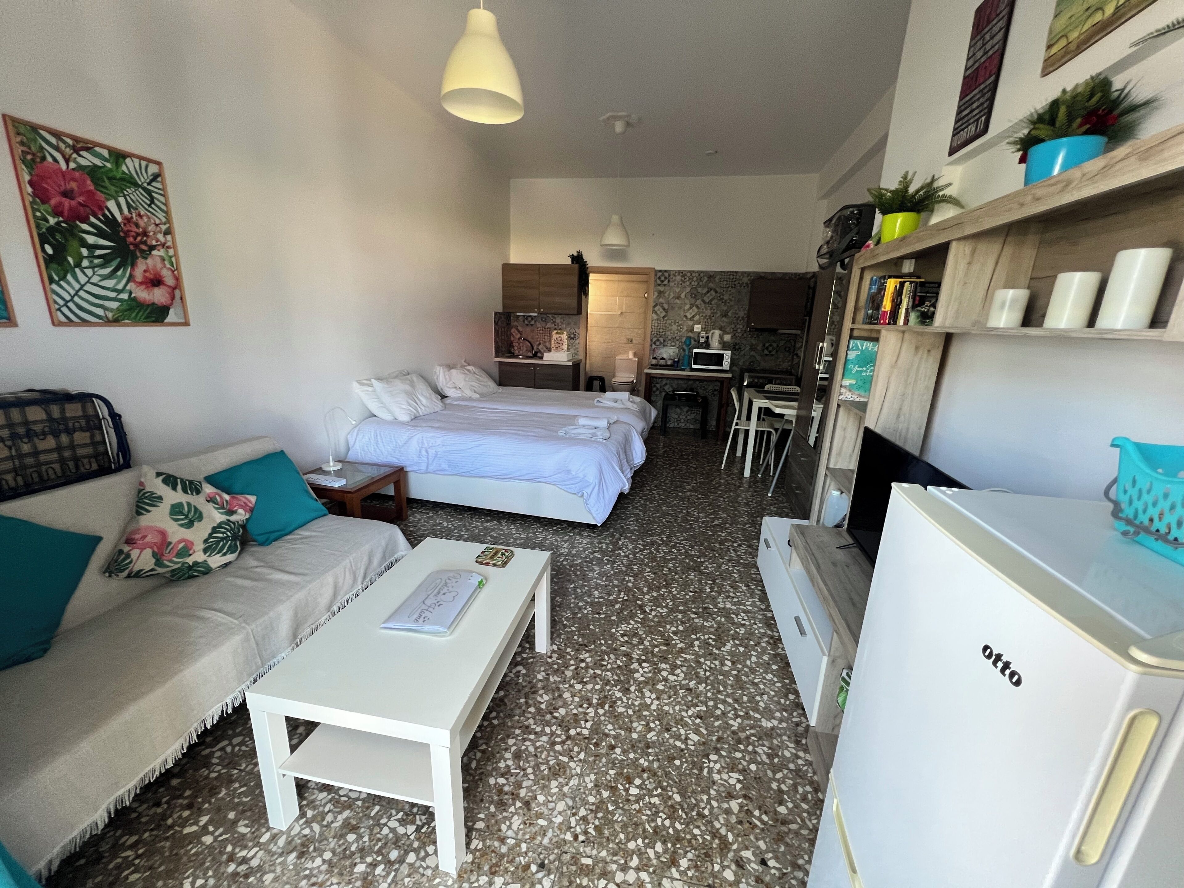 Een compacte hotelkamer met een bed, een bank, een klein bureau en een kitchenette.