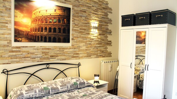 A bedroom with a bed, a nightstand, a wardrobe, and a picture of the Colosseum. - 50 Steps Colosseum Apartment (Roma)