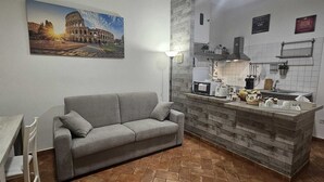 A compact kitchen with a grey sofa, a dining table, and a tiled backsplash. - 50 Steps Colosseum Apartment (Roma)