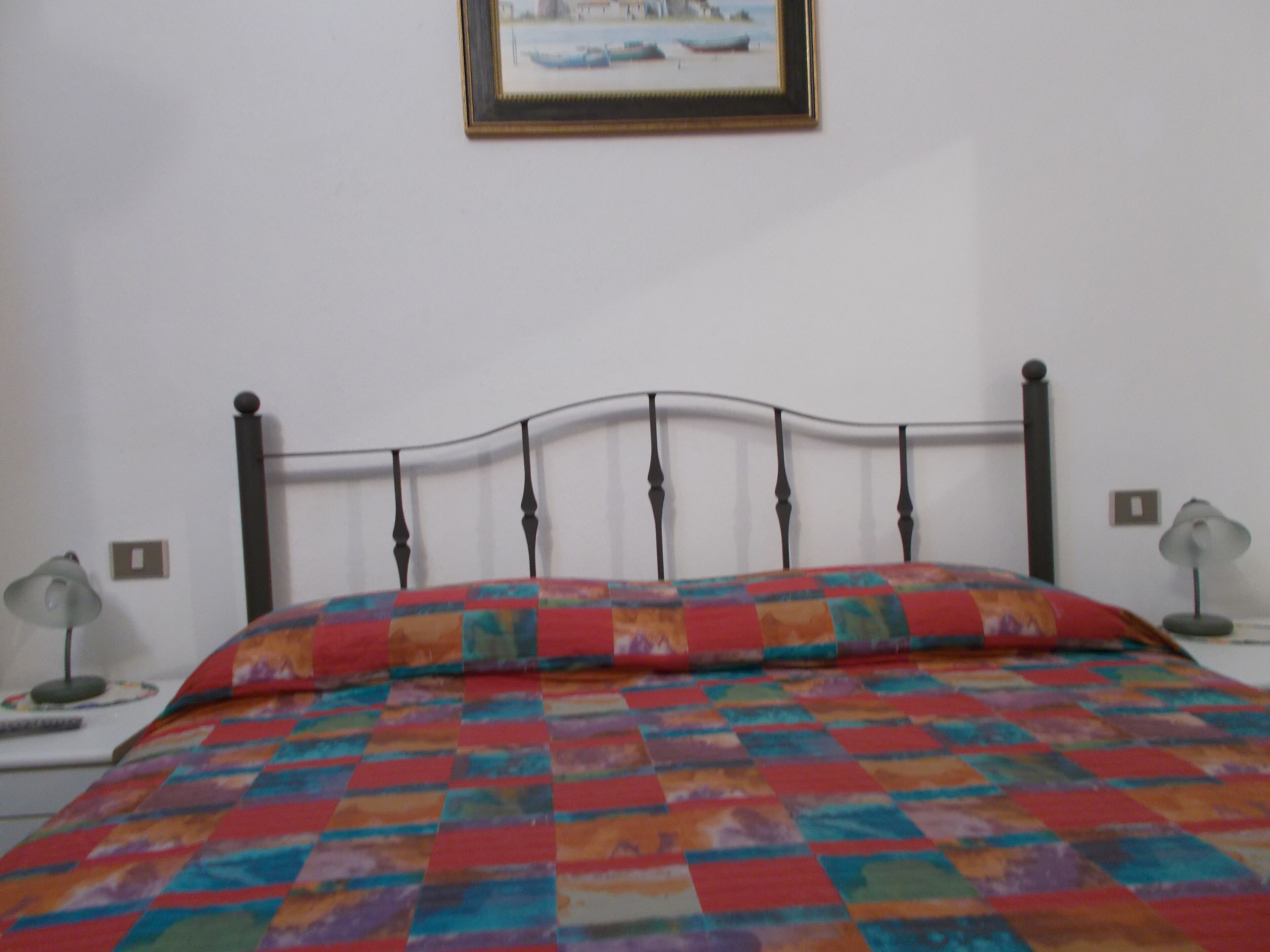 A bed with a colorful quilt, a metal headboard, and two bedside lamps.