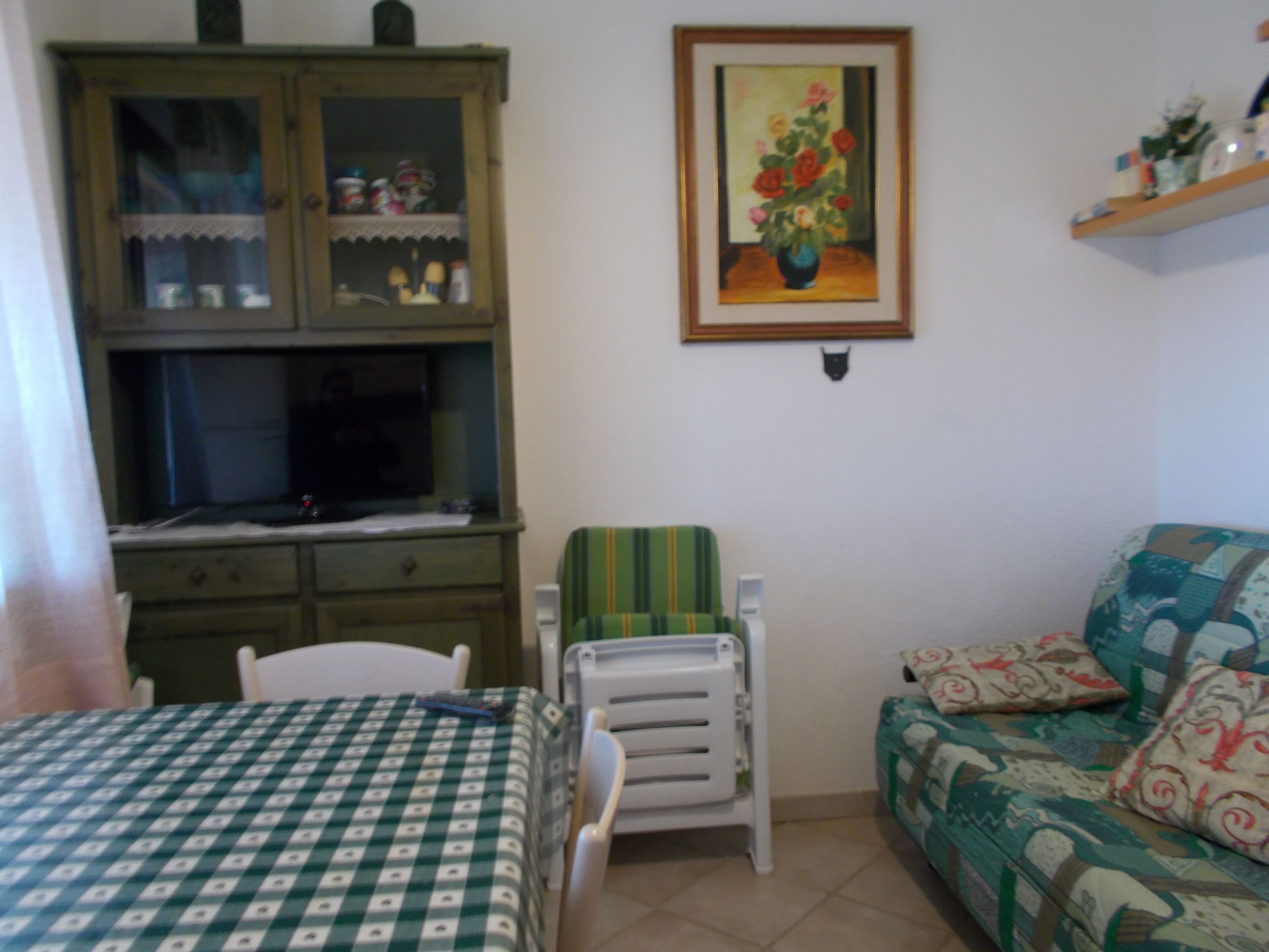 A room with a bed, a green cabinet, a chair, a sofa, and a painting on the wall.