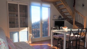Una sala de estar acogedora con un sofá, una mesa de comedor con sillas, una escalera y un aparador de vidrio con diversos objetos.