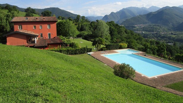 Una villa roja con piscina, rodeada de colinas y montañas verdes y exuberantes.