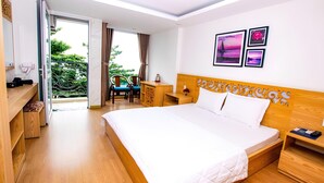 Une chambre d’hôtel avec un grand lit, une tête de lit en bois, un bureau avec une chaise et un balcon donnant sur un paysage verdoyant.