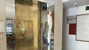 L’entrée d’un hôtel, avec un écran numérique indiquant l’étage de l’ascenseur, un paillasson et des affiches d’information accrochées au mur.