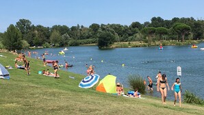 Ein Seeufer mit Menschen, die im Gras entspannen, einige im Wasser schwimmen, und ein paar Booten.