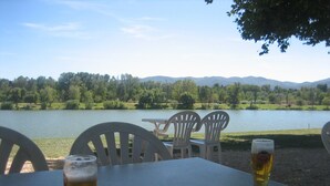 Ein Tisch mit zwei Biergläsern und einer Sonnenbrille, mit Blick auf einen See, Bäume und Berge im Hintergrund.