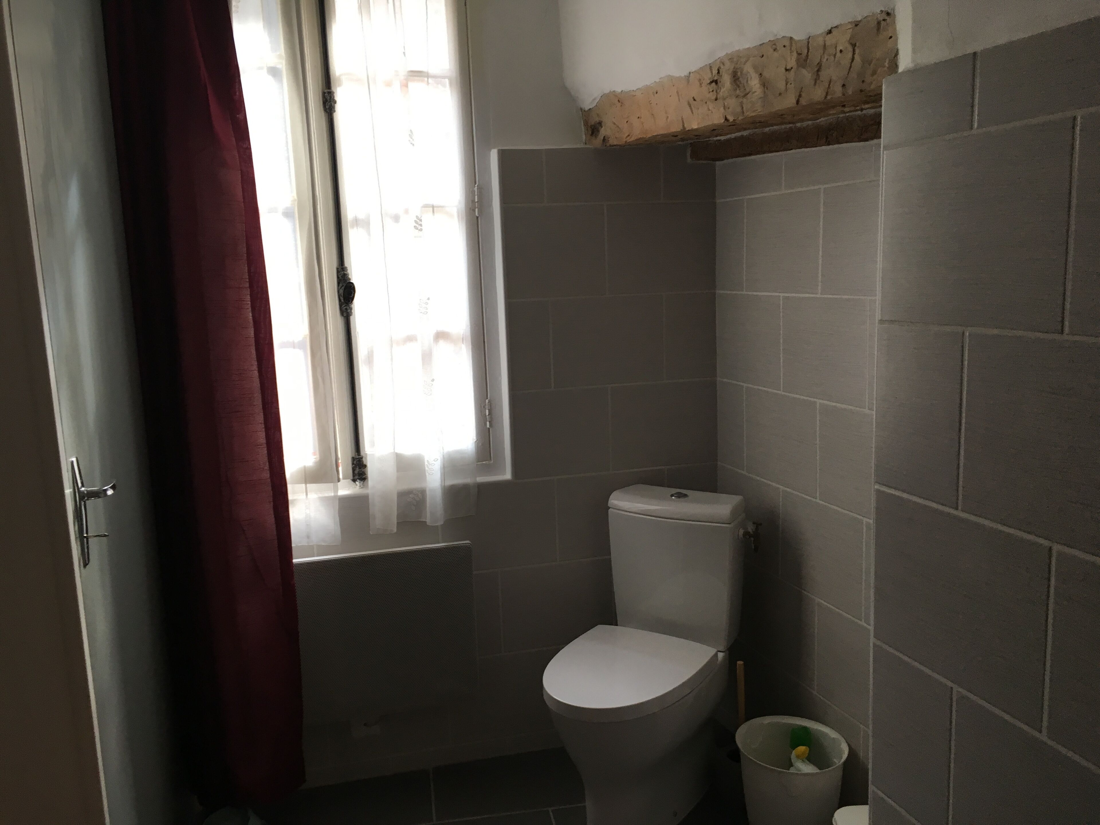 A small bathroom with a toilet, a window with curtains, and tiled walls.