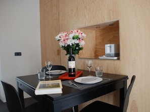 Una mesa de comedor con una botella de vino, copas, un libro y un arreglo floral.