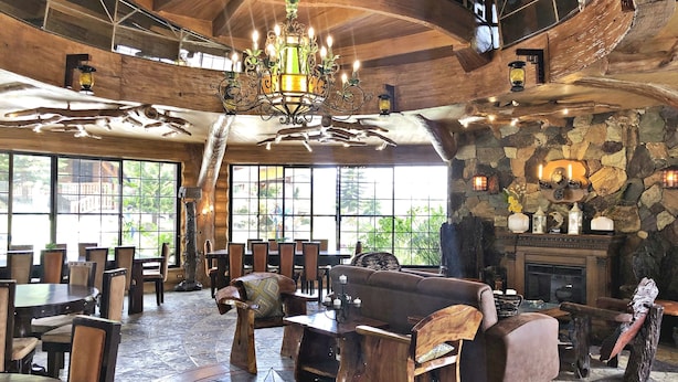 A spacious lobby with wooden furniture, a large chandelier, stone walls, and large windows offering views of greenery.
