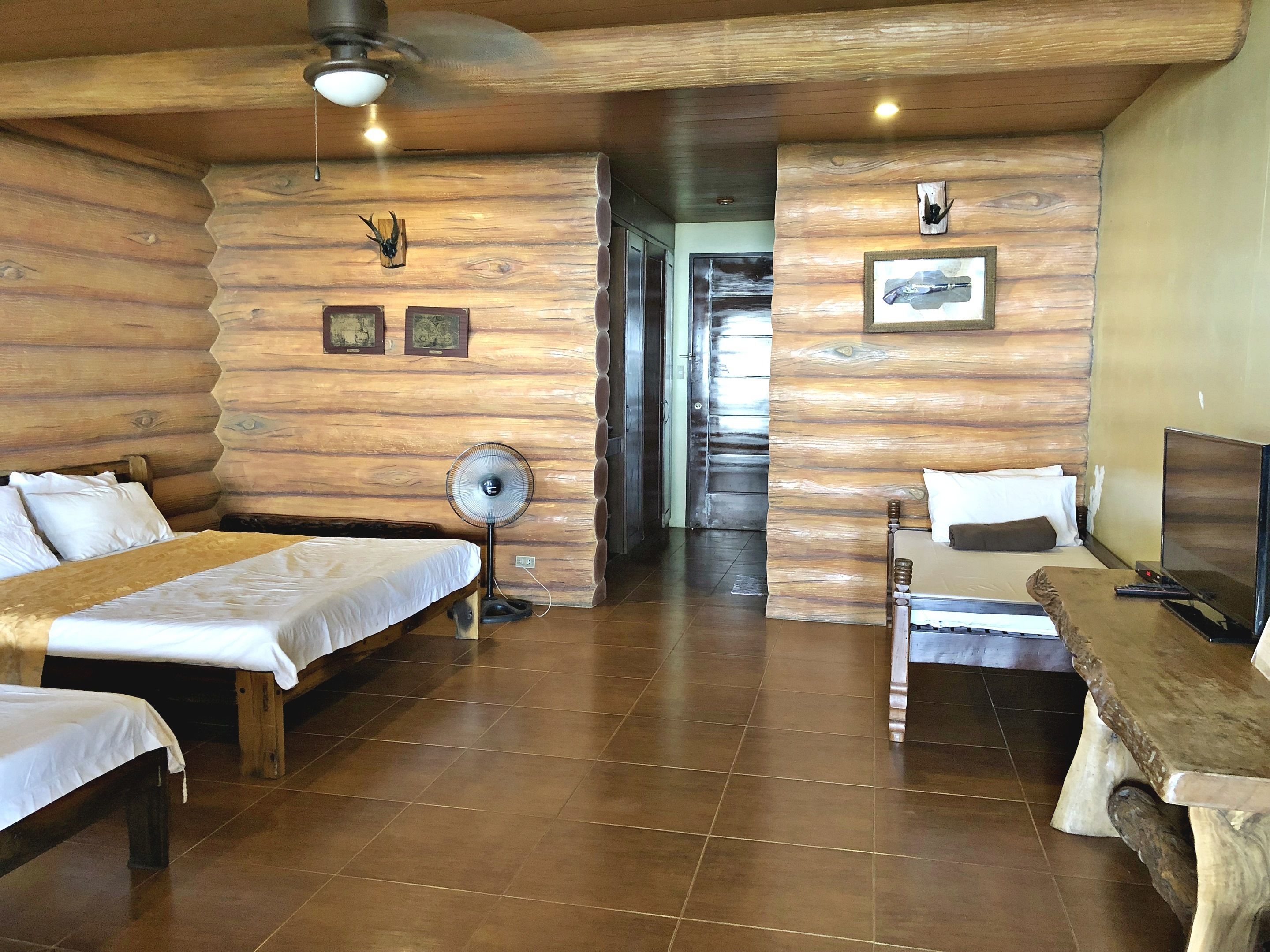 Quarto estilo cabana de tronco com duas camas, um ventilador, uma TV e paredes de madeira.