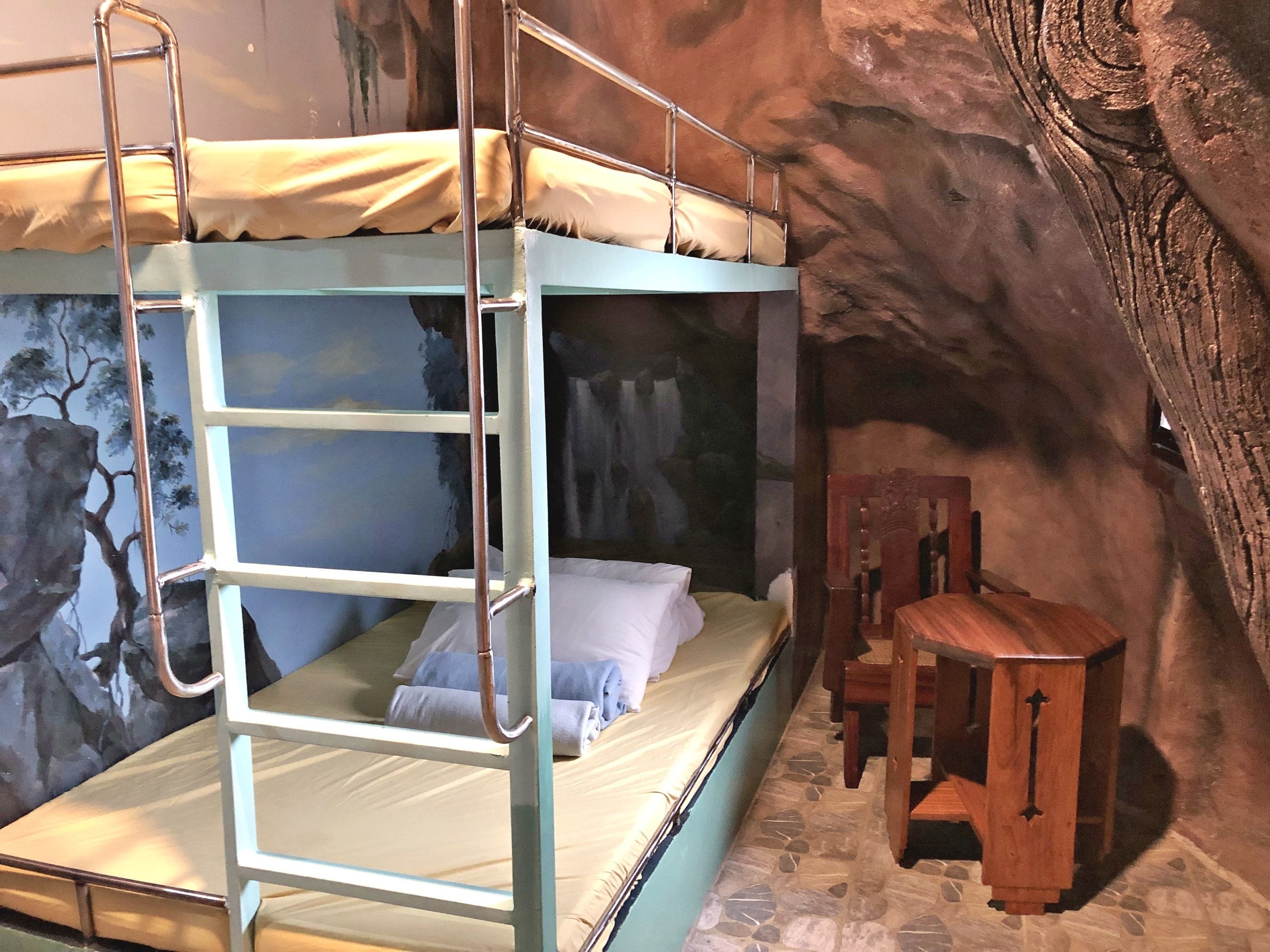 Una cama litera con escalera, una silla de madera y una pared de piedra.